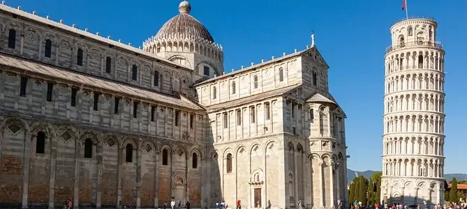 The Leaning Tower of Pisa and the Pisa Cathedral on a clear day with tourists visible in the foreground.