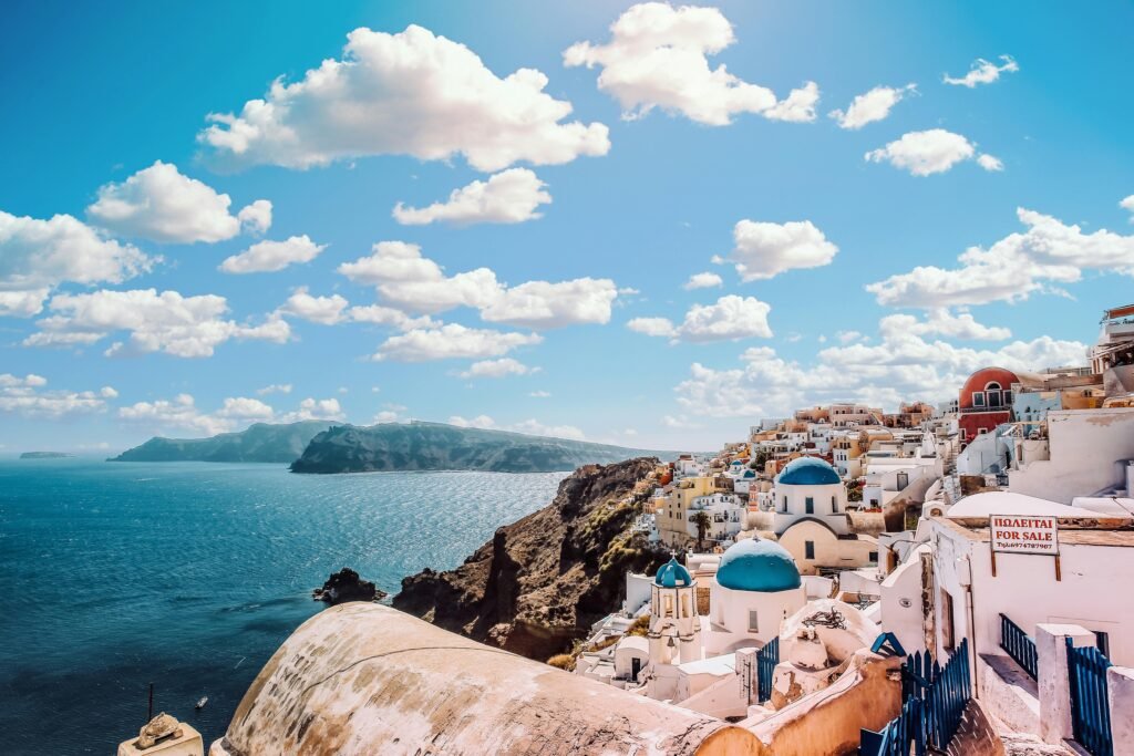 A panoramic view of Santorini, Greece, showcasing the iconic white buildings with blue domes overlooking the Aegean Sea under a clear blue sky.