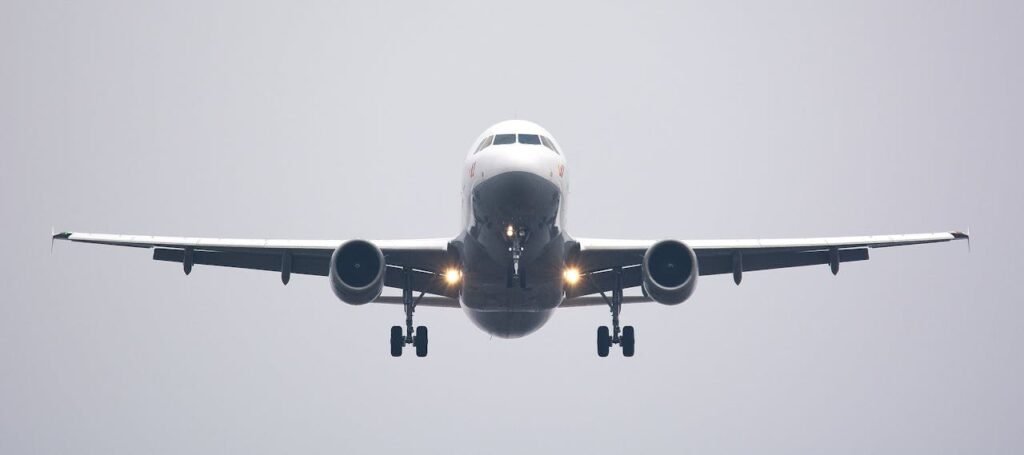 A commercial airplane in mid-flight with landing gear extended, approaching head-on against a clear sky.