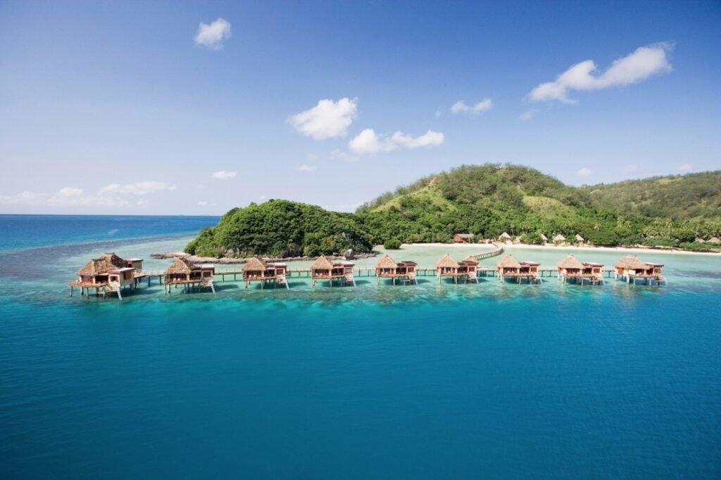 Aerial view of Likuliku Lagoon Resort in Fiji, showcasing over-water bungalows and surrounding clear blue waters.