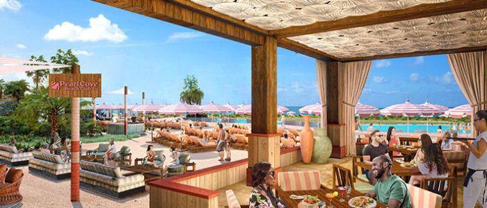 Open-air dining area at Pearl Cove with patrons enjoying meals under a patterned wooden ceiling, overlooking a sandy beach with umbrellas and loungers.