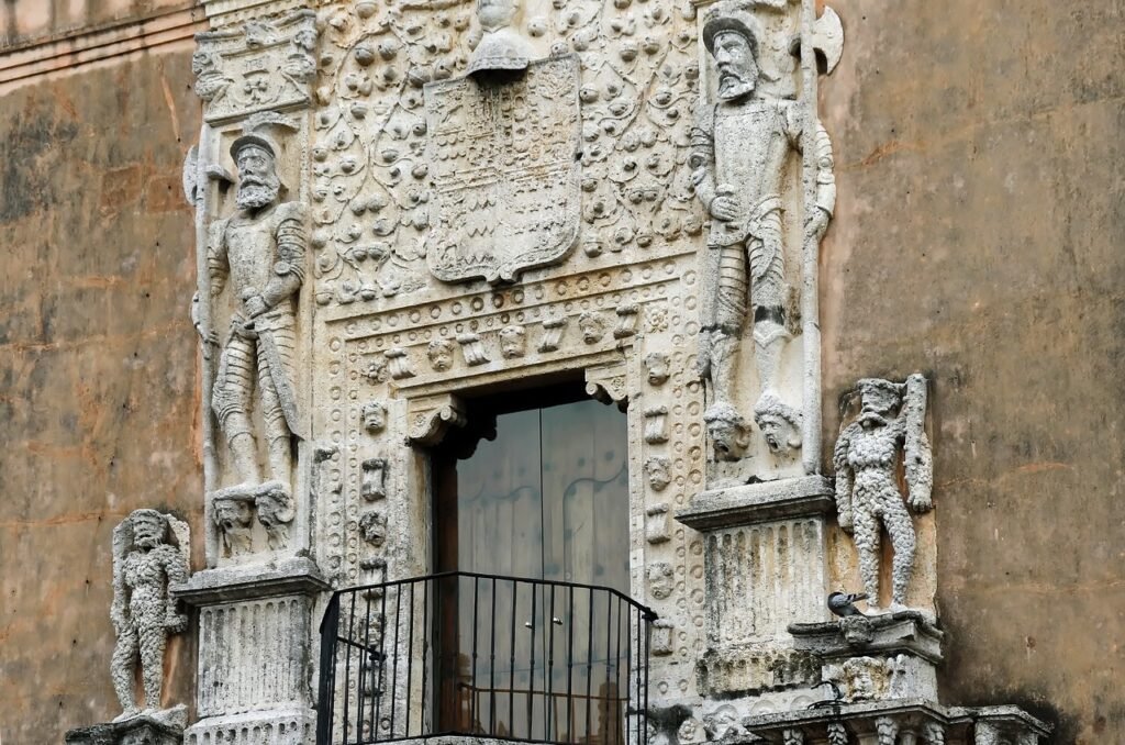 mexico, merida, yucatan. An intricately carved stone doorway flanked by two sculpted figures, with a balcony above featuring ornate railings. Mayan sites Yucatán Peninsula