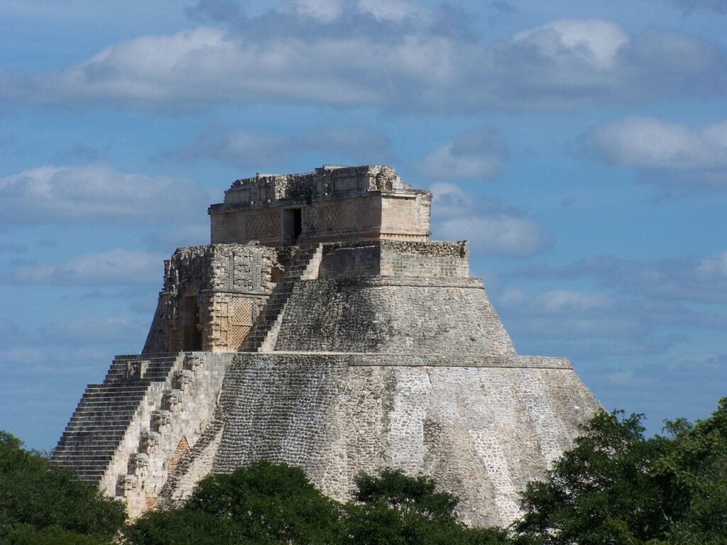 A photo of the Pyramid of the Magician, a pre-Columbian step pyramid located in Uxmal, Mexico, under a partly cloudy sky.