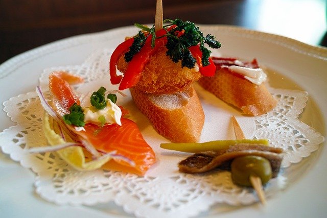 Unique travel destination San Sebastián with a variety of pintxos. A close-up image of a variety of pintxos, traditional Basque appetizers, on a white plate with a lace paper doily.