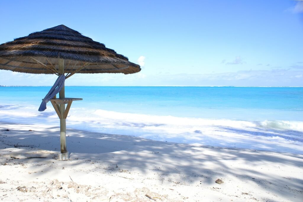 Thatched beach umbrella on the pristine white sands of Turks and Caicos with clear turquoise ocean in the background.