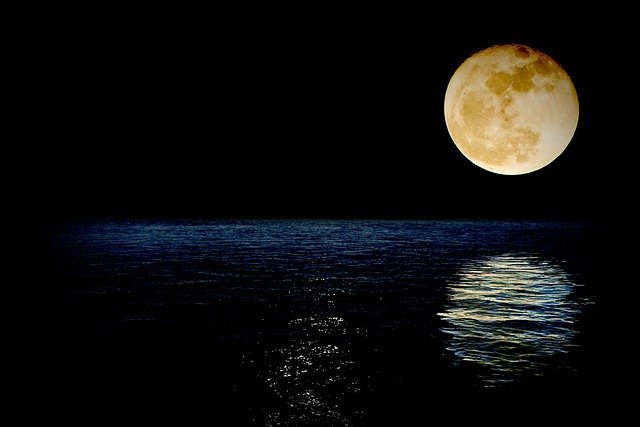 A full moon illuminating the dark night sky and reflecting on the calm sea.