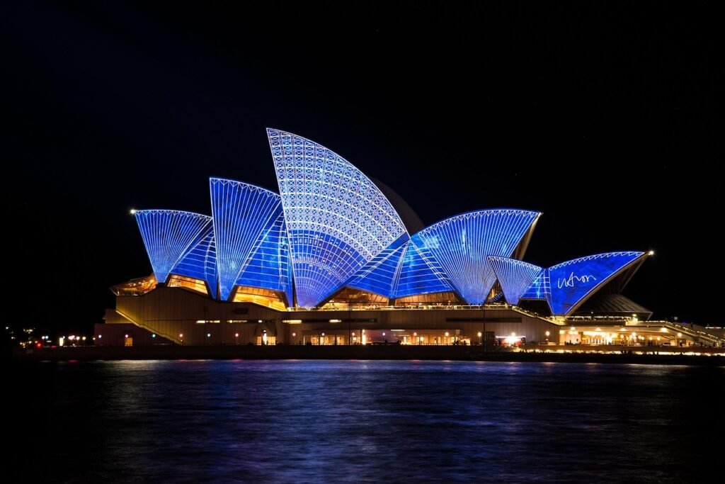 Sydney Opera House illuminated with blue lights at night, reflecting on the waterfront. Trending Travel Destinations 2024