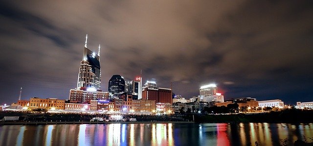 Nighttime panorama of Nashville’s skyline with prominent buildings lit up and their reflections on the Cumberland River.