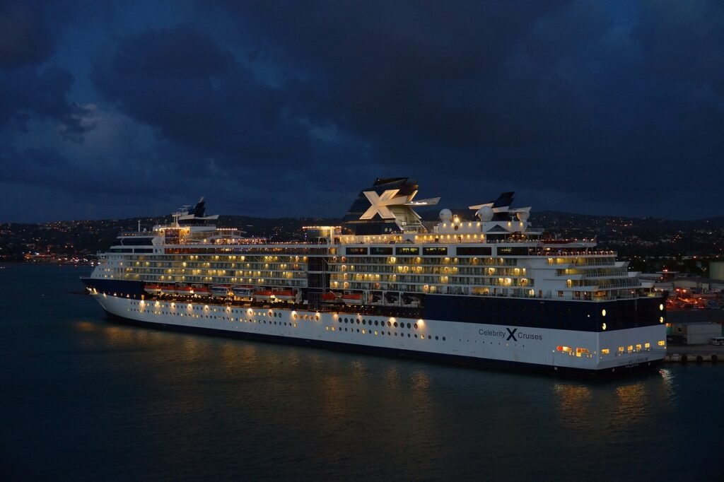 Illuminated Celebrity cruise ship docked at twilight with lit windows reflecting on calm waters.