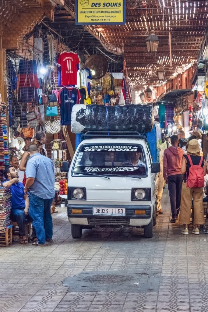 Bustling Moroccan market street with goods displayed and a white van parked in the center.  Trending travel destinations 2024.