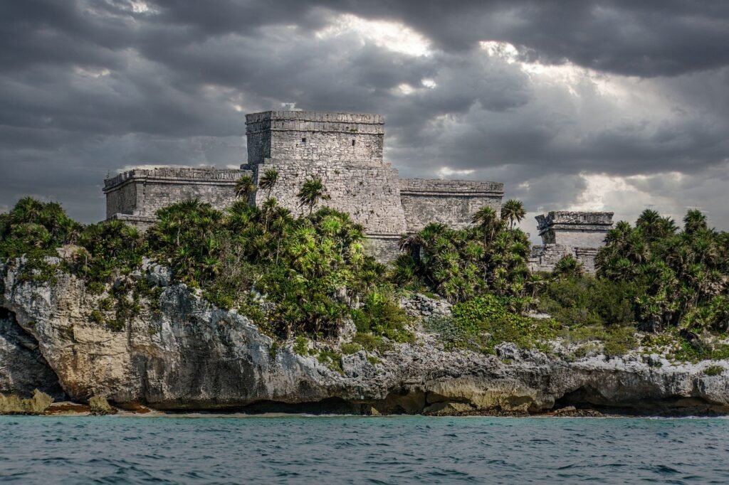 Ancient Mayan ruins of Tulum perched on a cliff overlooking the Caribbean Sea, with lush green vegetation and a dramatic sky. Mayan sites Yucatán Peninsula