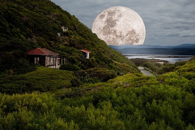 An oversized full moon looms behind a hillside with abandoned buildings, creating a dramatic and surreal landscape.