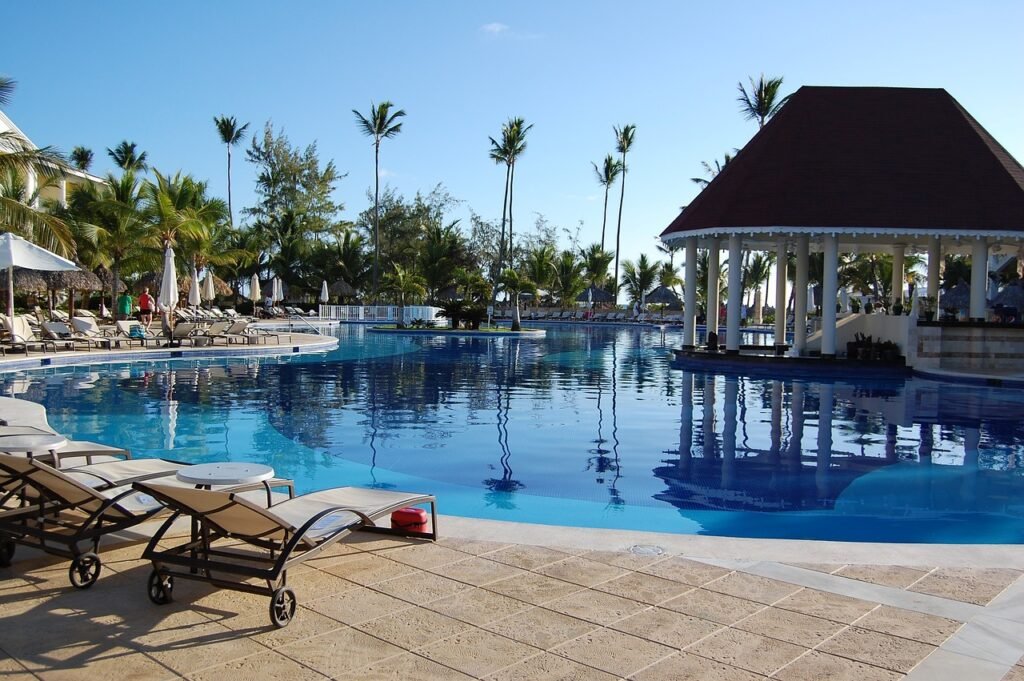 Luxurious resort swimming pool in the Dominican Republic with sun loungers, palm trees, and a gazebo under a clear blue sky.