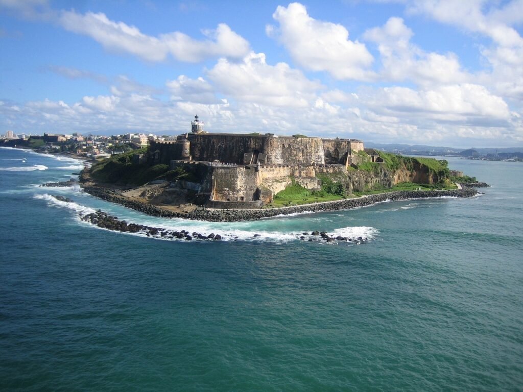 Aerial view of Castillo San Felipe del Morro, an iconic 16th-century fortress in San Juan, Puerto Rico, surrounded by turquoise waters and rocky shores with the city skyline in the distance.