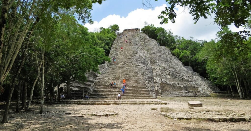 Visitors climbing the Nohoch Mul pyramid at Coba, surrounded by dense forest.