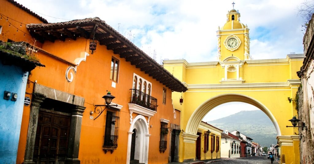 Santa Catalina Arch with clock tower on a sunny day in Antigua, Guatemala, showcasing colonial architecture and mountain backdrop.