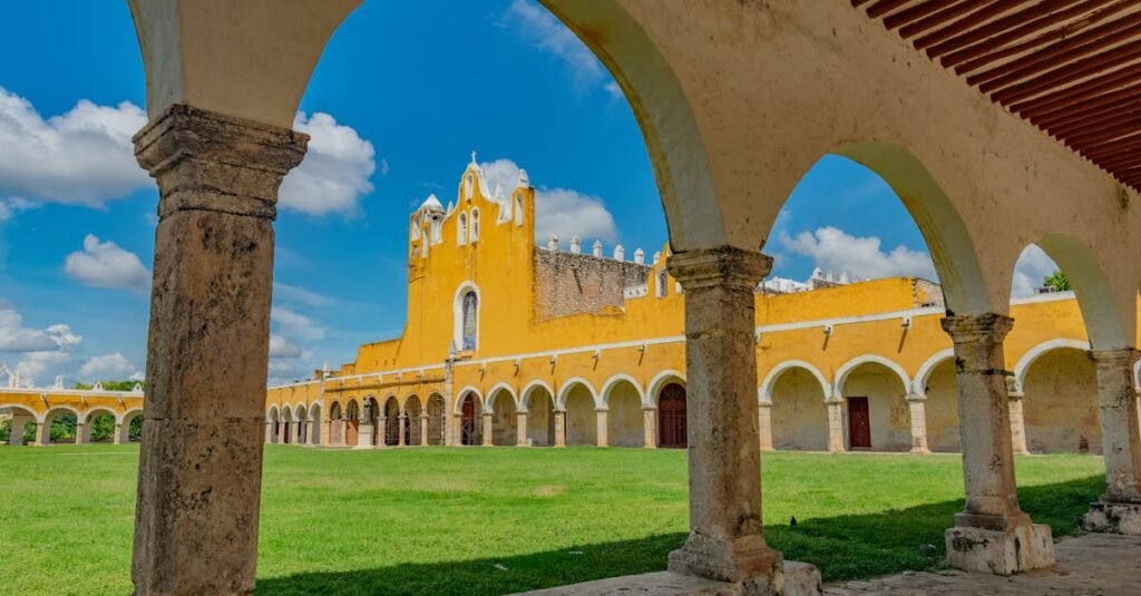 Mayan sites Yucatán Peninsula. Arcos en Izamal. A panoramic view of a historic yellow building with arched colonnades and a bell-gabled facade under a blue sky with scattered clouds.