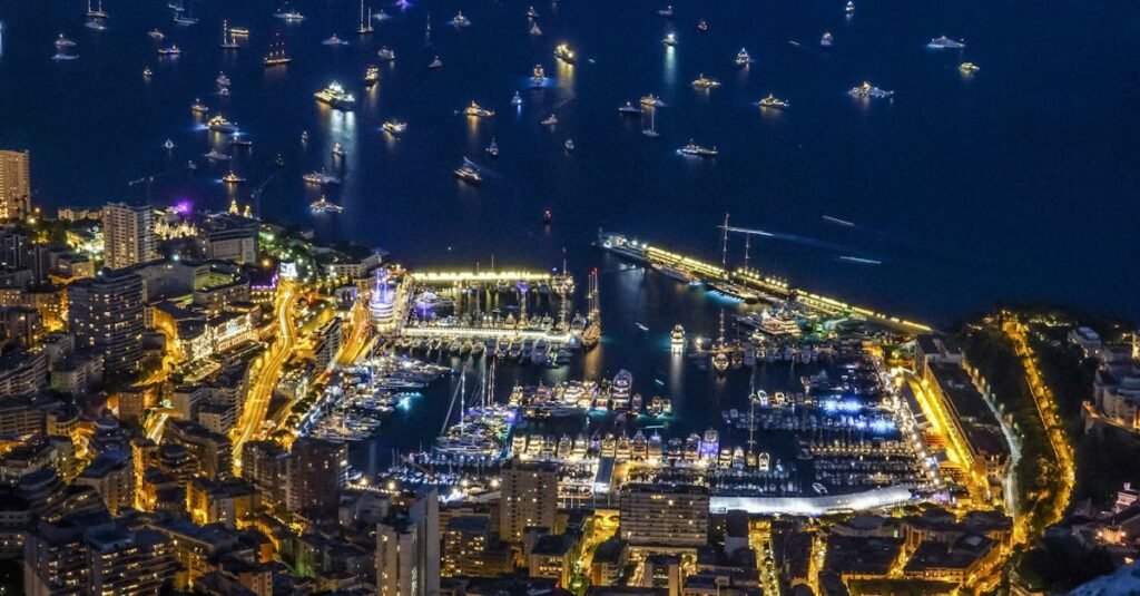 Aerial view of Monaco at night with a marina full of boats and surrounding city lights.