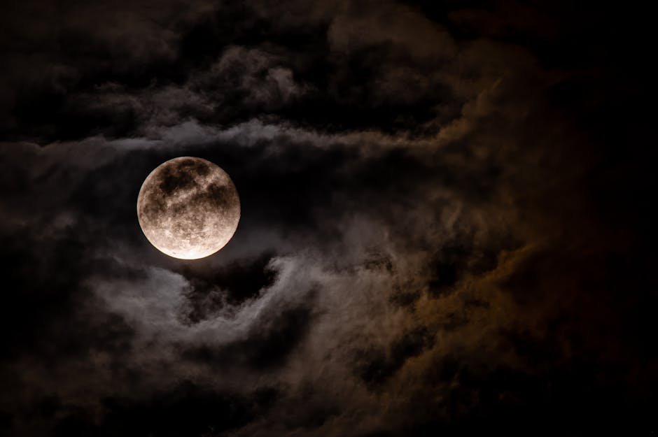 Full moon with visible craters against a dark cloudy night sky.