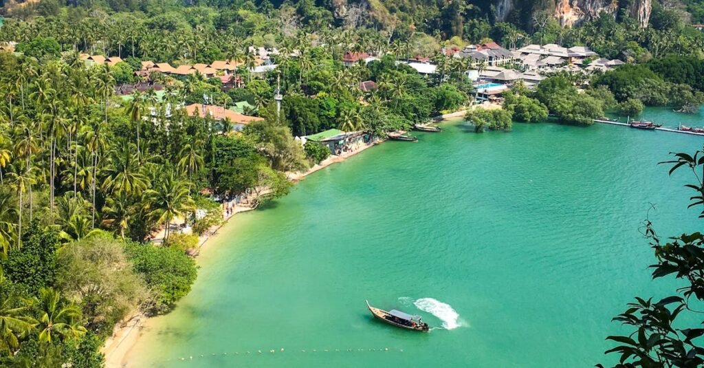 High-angle view of Railay Beach in Thailand with turquoise water, lush greenery, and a long-tail boat near the shore.