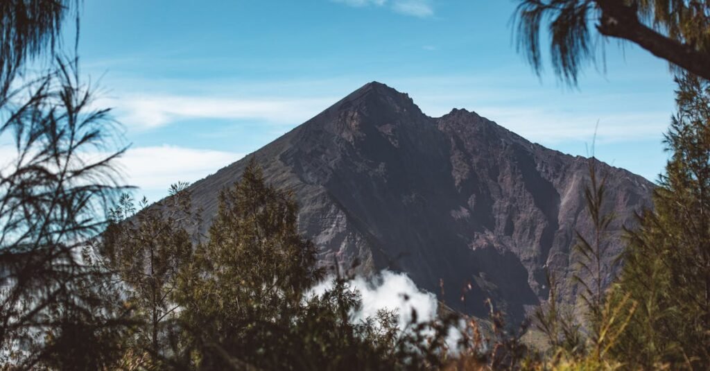 View of Mount Rinjani’s peak with surrounding foliage and clouds at its base under a clear blue sky.