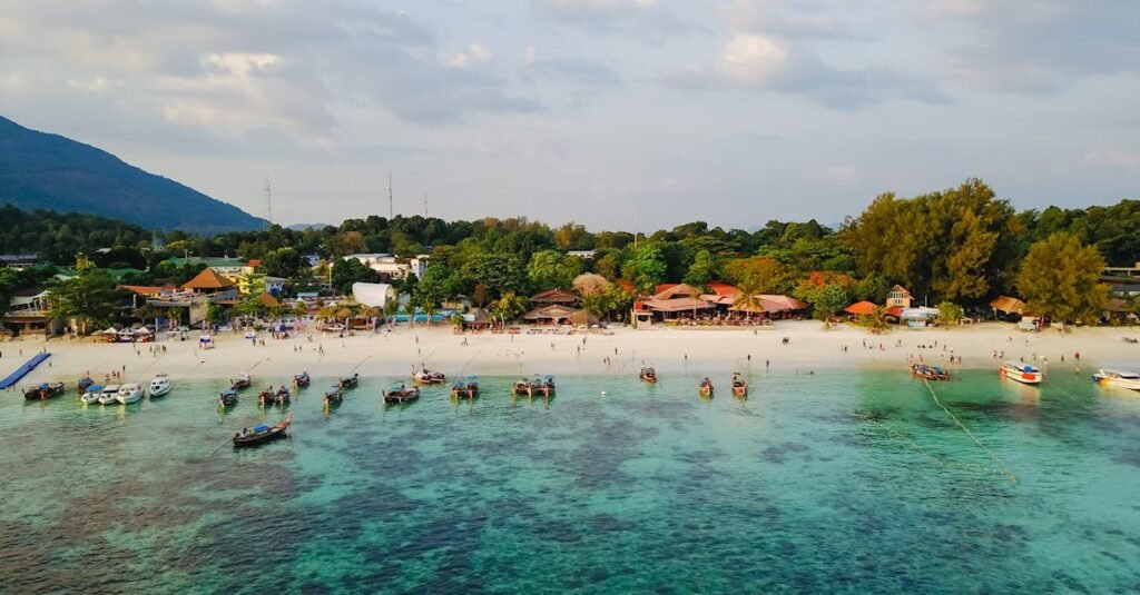 Turquoise waters and boats near a beach lined with resorts in Thailand.