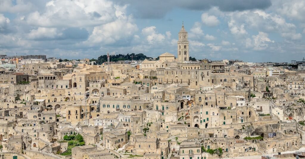 Panoramic view of Matera, featuring ancient cave dwellings and stone structures under a cloudy sky.