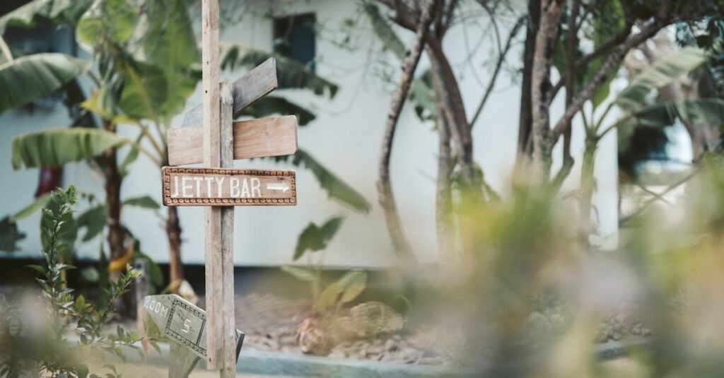 Wooden signpost with directional signs, including ‘JETTY BAR,’ in St. Kitts with foliage and a white building in the background.