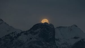 Glowing full moon rising behind a snow-capped mountain on a clear night