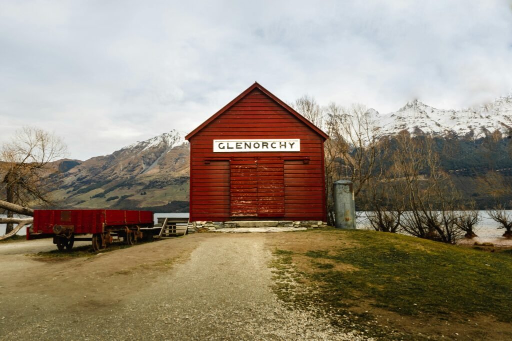 A red wooden building with the sign "GLENORCHY" in a scenic mountainous area with a lake in the background.