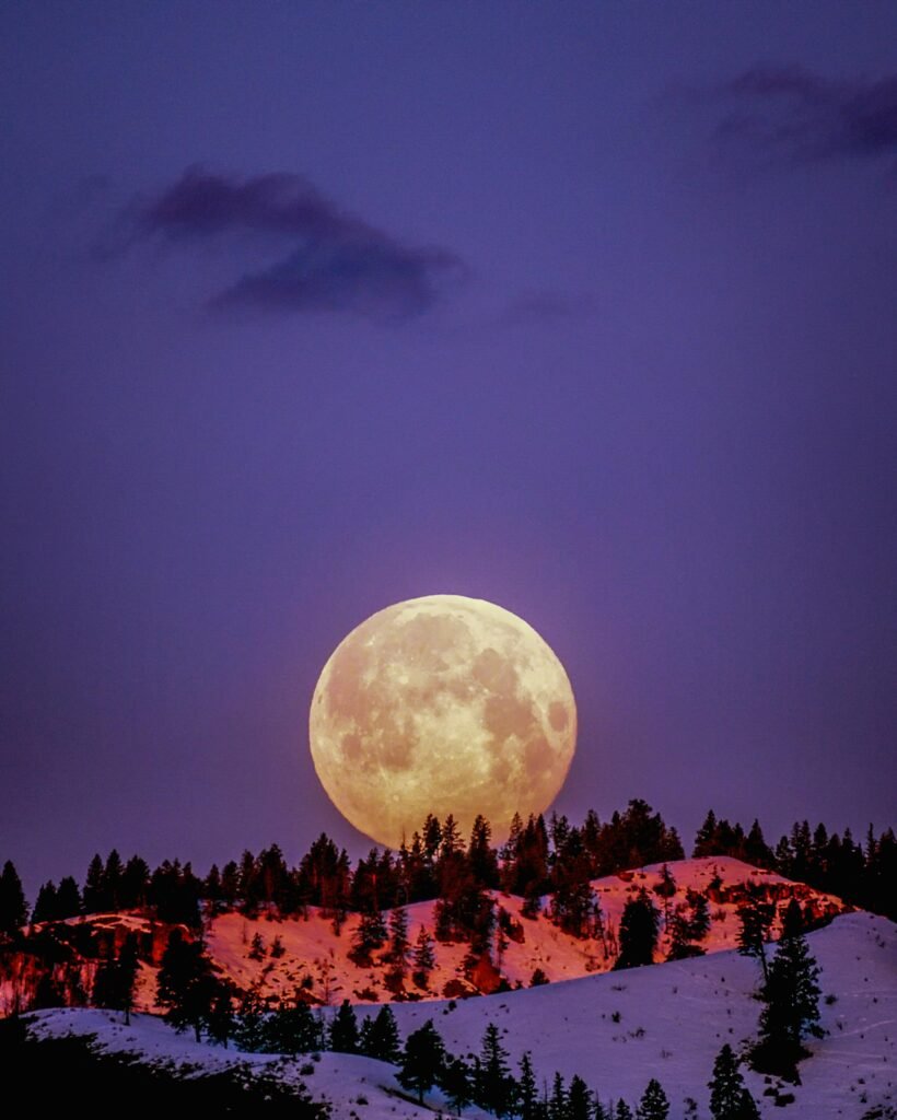 Full moon rising over snow-covered hills during twilight.