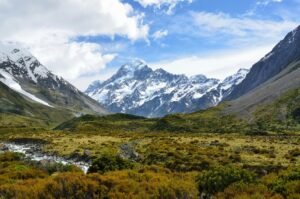 A panoramic view of Mount Sunday with towering snow-capped peaks and lush green valleys under a clear blue sky.