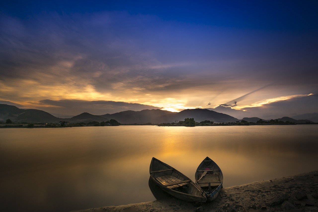 Two wooden boats on a calm lake at sunset with mountains in the background. Kindness and Boundaries