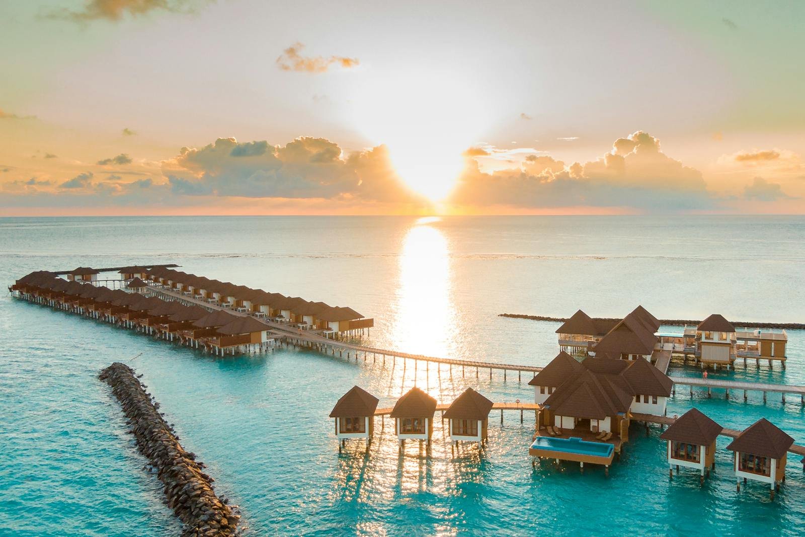 Captivating aerial view of luxurious Maldives overwater bungalows and villas at sunrise, reflecting on a calm ocean, perfect for a serene vacation.