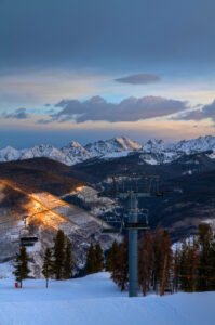 Ski lift foreground at sunrise over snow-covered Vail Mountain with evergreen trees and clear blue skies