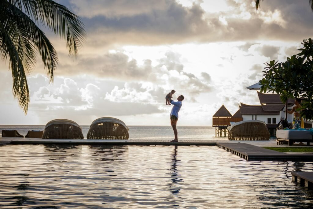 A person holding a child near a pool with a scenic ocean view in the Maldives.